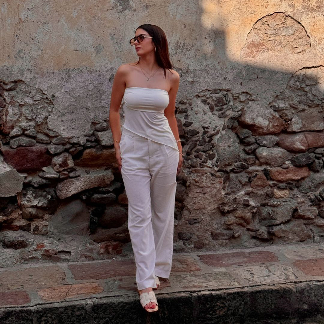 Person in white outfit standing against a textured stone wall.